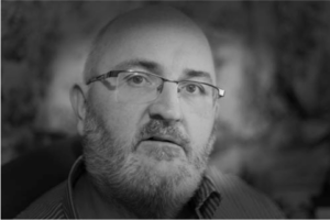 A black and white photo of a man with glasses and a beard.