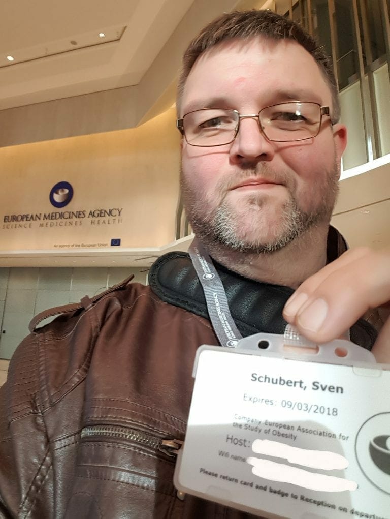 A man holding up his id card in front of a building.