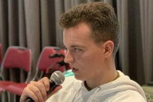 A young man in a white hoodie holding a microphone.