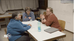 Three women sitting at a table talking to each other.