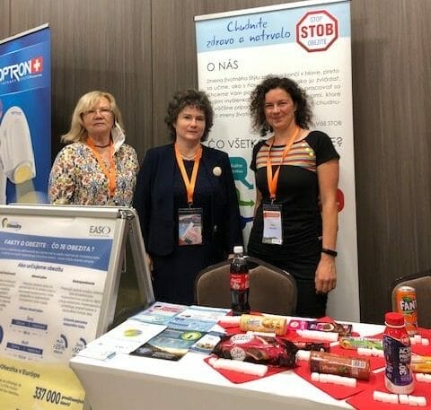 Three women standing in front of a table at a conference.