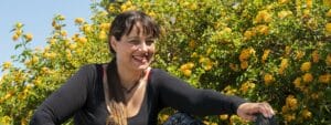 A woman posing in front of a bush with yellow flowers.