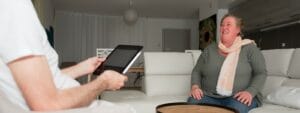 A woman sitting on a couch talking to a man on a tablet.