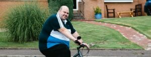 A bald man riding a bike in front of a house.