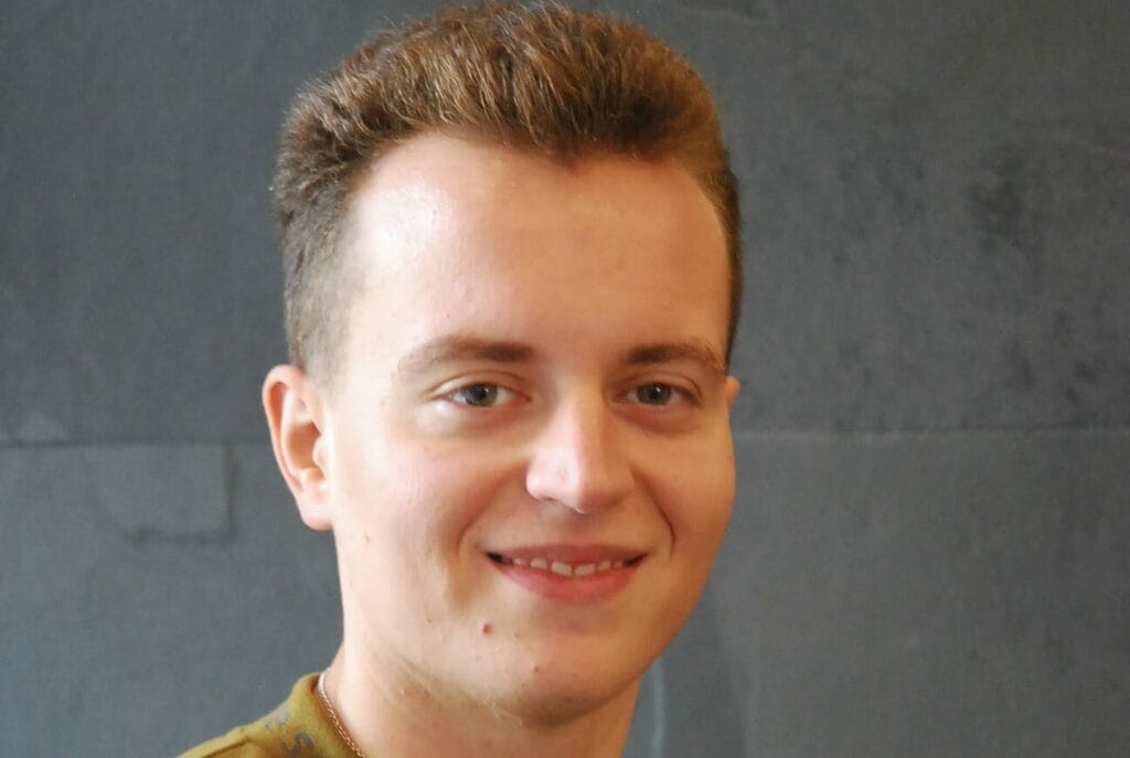 A man in a camouflage shirt smiles for the camera.