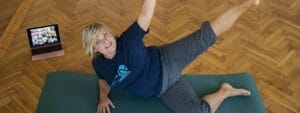 A woman doing yoga on a mat with a laptop.