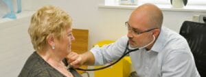 A man is examining an elderly woman with a stethoscope.