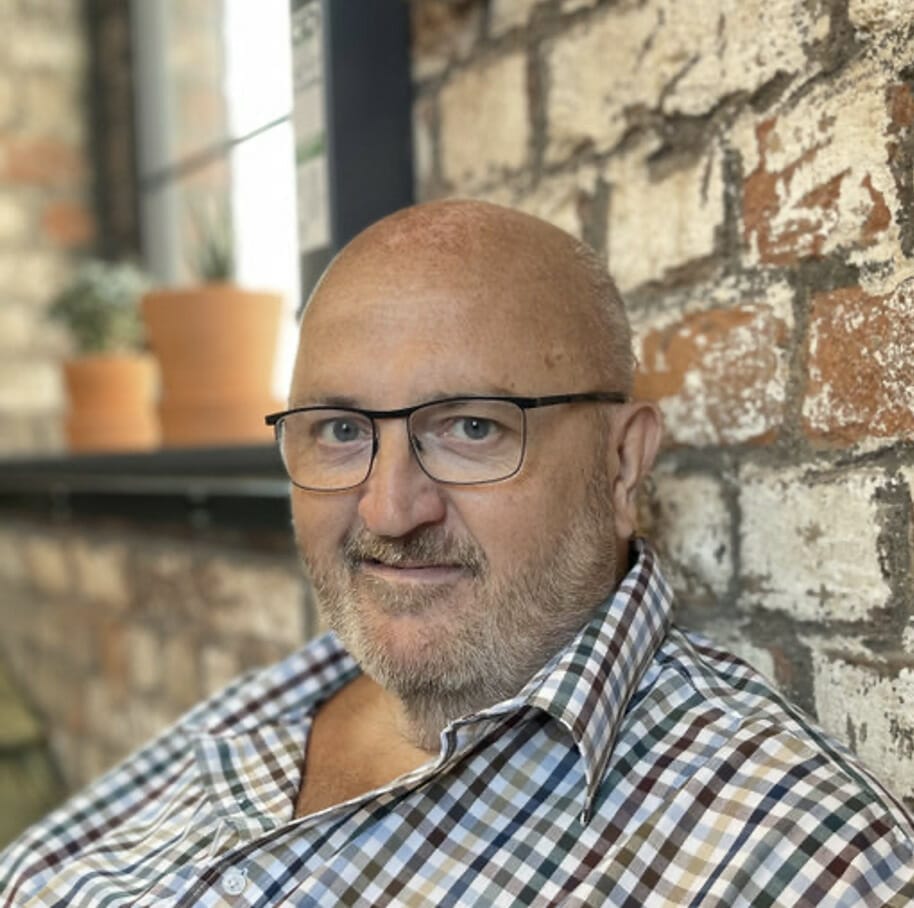 A bald man wearing glasses and a checkered shirt.