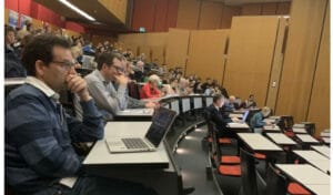 A group of people sitting in a lecture hall with laptops.