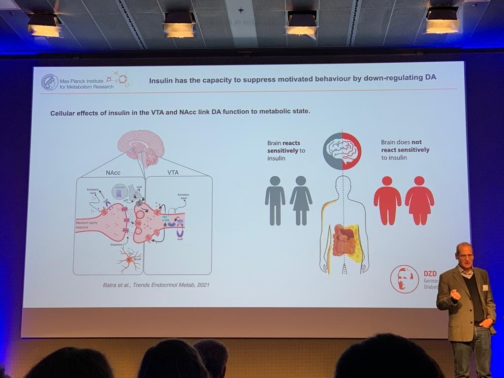 A man is standing in front of a screen showing a presentation.