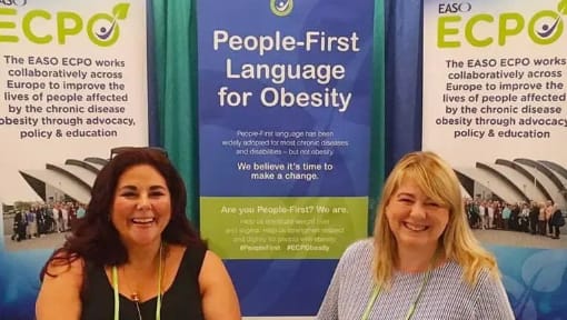 Two women standing in front of a booth that says people first language for obesity.
