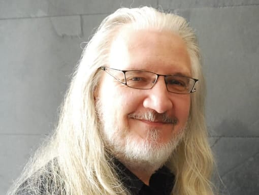 A man with long hair and glasses smiling for the camera.