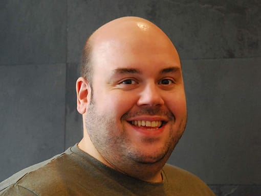 A man smiling in front of a wall.