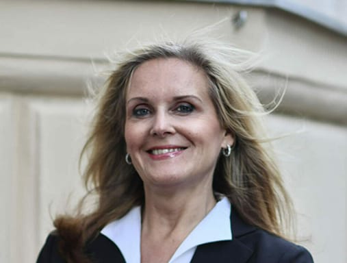 A woman in a business suit smiling in front of a building.
