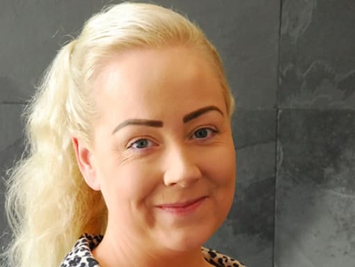 A woman with blonde hair smiling in front of a wall.