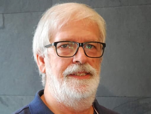 A man with glasses and a beard standing in front of a wall.