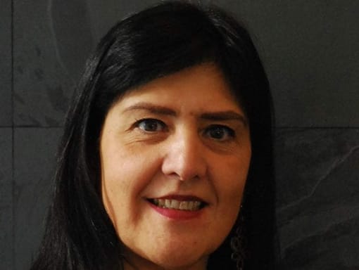 A woman with long black hair smiling in front of a wall.