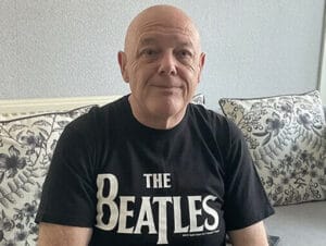 A man sitting on a couch wearing a beatles t - shirt.