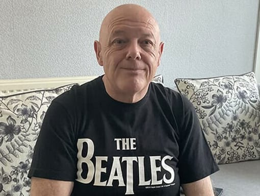 A man sitting on a couch wearing a beatles t - shirt.