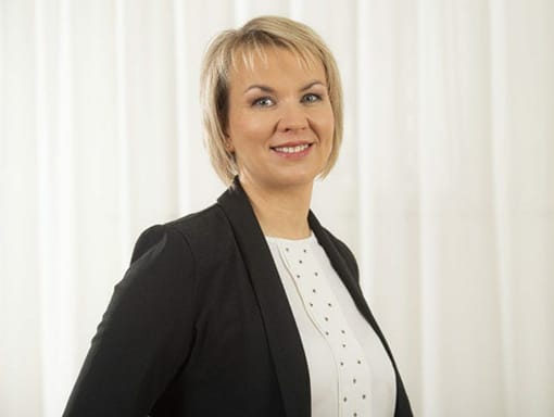 A woman in a black blazer is smiling in front of a curtain.