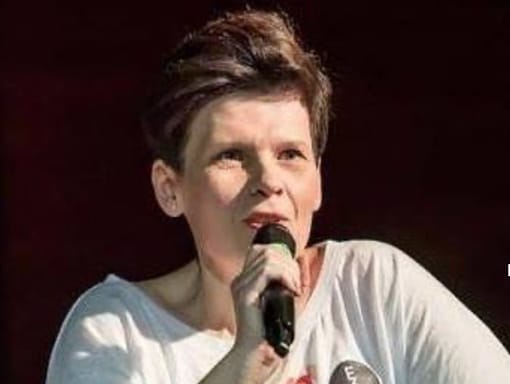 A woman in a white shirt speaking on a microphone.