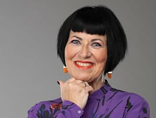 A woman with short black hair wearing a purple shirt and orange earrings.