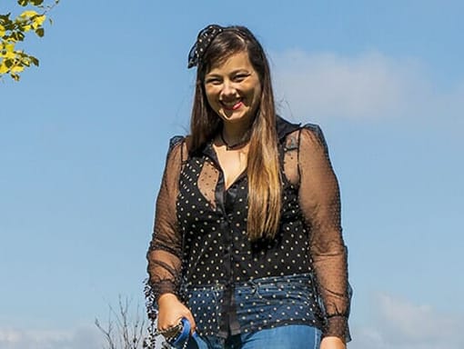 A woman wearing jeans and a polka dot blouse standing in a field.