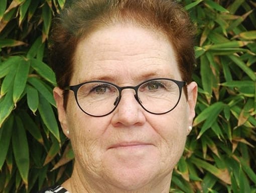 A woman in glasses is standing in front of a bush.