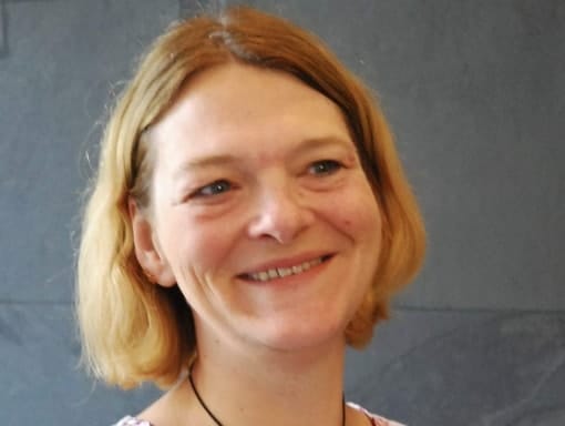 A woman with blonde hair smiling in front of a gray wall.