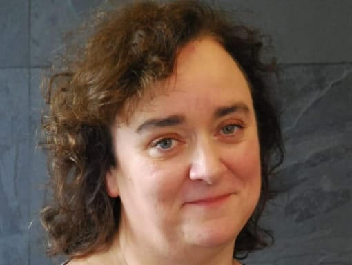 A woman with curly hair standing in front of a wall.