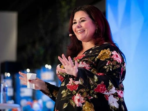 A woman in a floral dress is giving a speech.