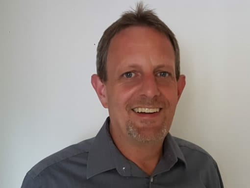 A man smiling in front of a white wall.