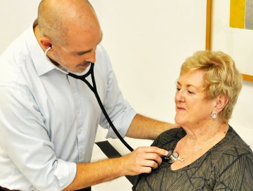 A doctor is checking an elderly woman's stethoscope.