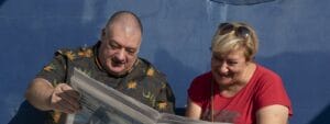 A man and woman reading a newspaper in front of a blue wall.