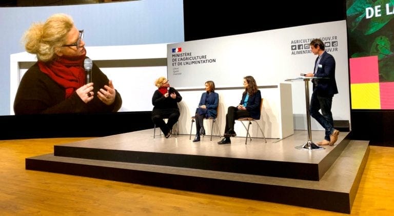 A woman speaking to a group of women on a stage.