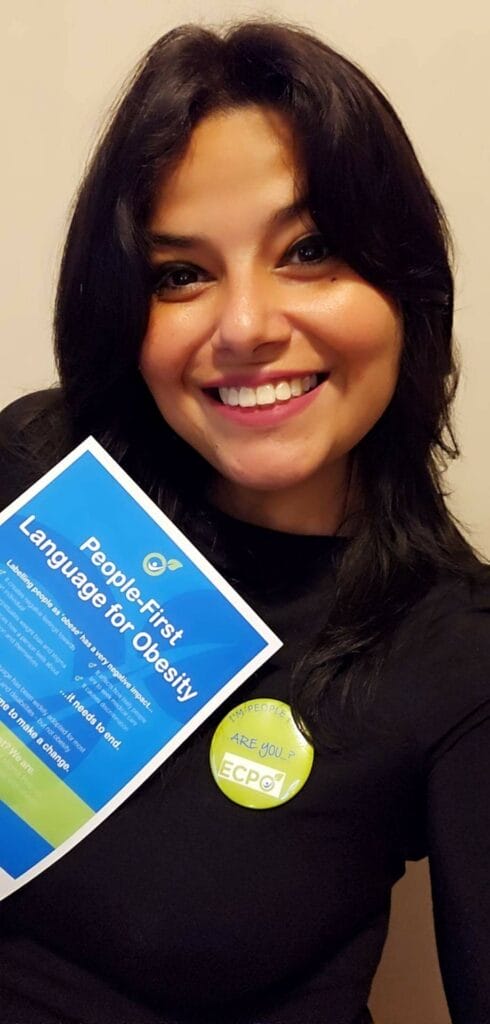 Person smiling and holding a flyer titled "People-First Language for Obesity," wearing a button that says "ECP.