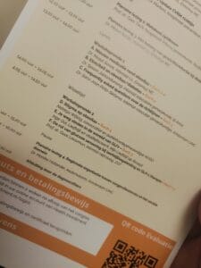 Close-up of a conference schedule printed on paper, listing workshops, sessions, times, and locations. A QR code for evaluation is visible at the bottom right.