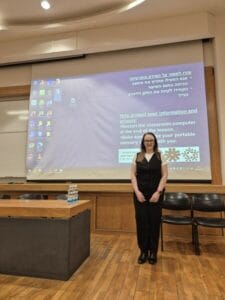 A person standing in a classroom in front of a projection screen displaying computer desktop icons and a message about protecting information and privacy.