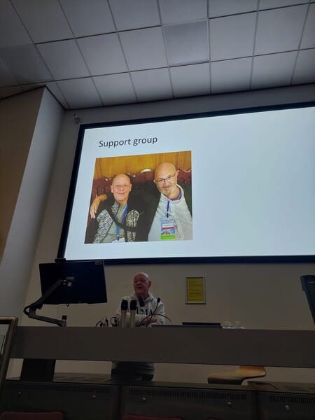 A person is giving a presentation with a slide titled "Support group," displaying a photo of two people smiling and posing together.