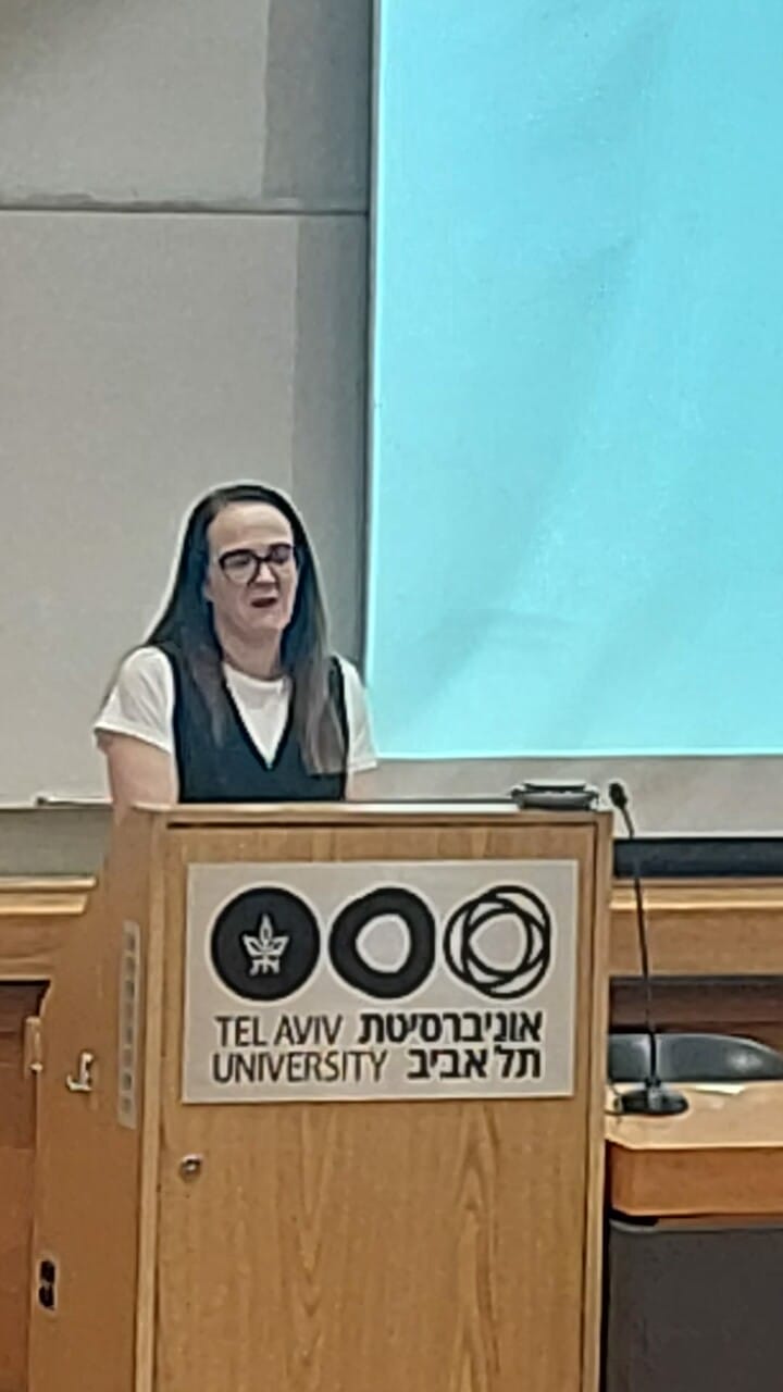 A person is speaking at a podium in a lecture hall at Tel Aviv University.