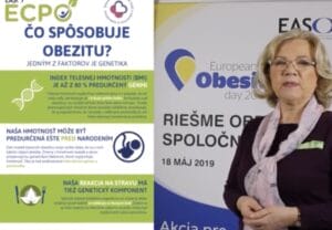 A woman stands next to a poster about obesity, genetics, and BMI, with text in Slovak and the date May 18, 2019, visible.