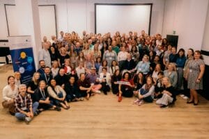 Large group of people posing together indoors, some seated on the floor and others standing, with a banner reading "#EUPATI" in front.
