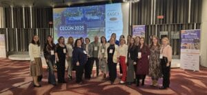 A group of people pose for a photo in front of a screen displaying information about the Central European Congress on Obesity 2025.